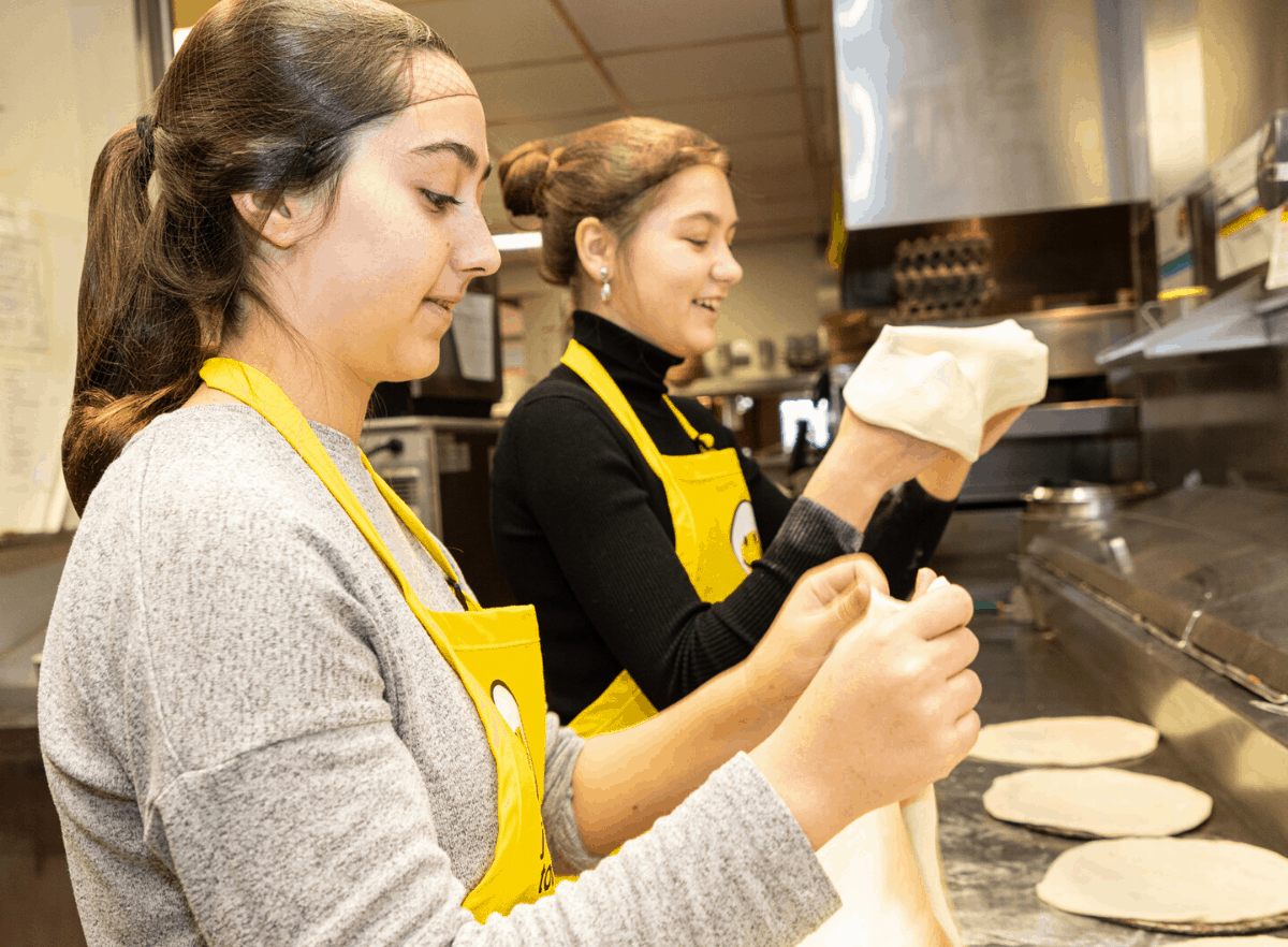 2 young women making pitas in a kitchen