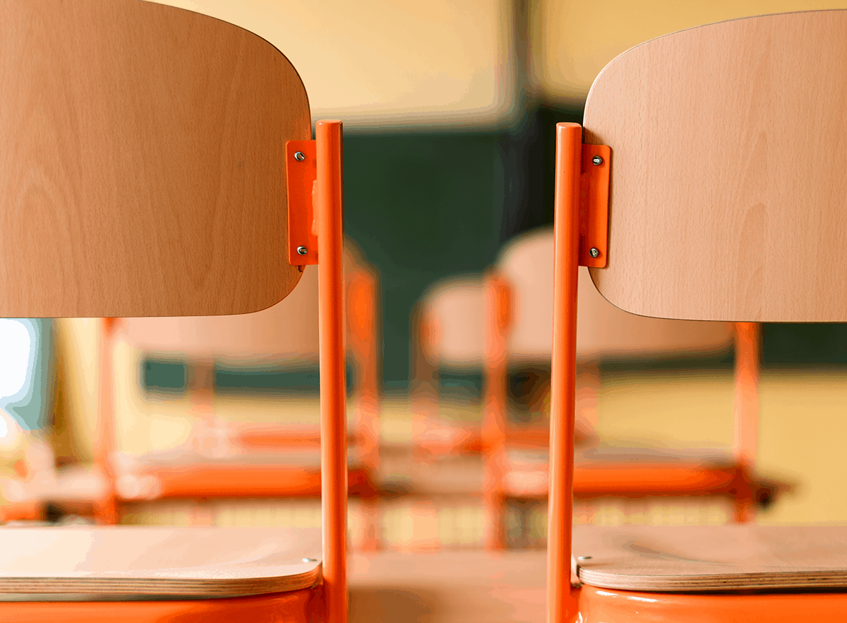 Chairs stacked up on desks with a blurred background of a classroom